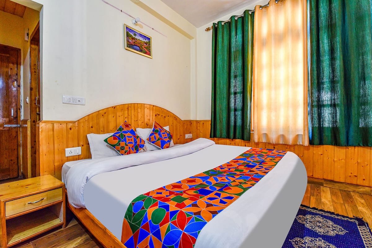 A wooden-paneled room with a bed, a nightstand, a power outlet, and a window with green curtains.