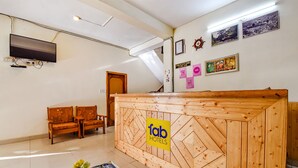 A reception desk with a wooden design and a 'fab hotels' sign, a television mounted on the wall, and a staircase leading to another floor. - Fabhotel Suvidha Cottage (Manali)