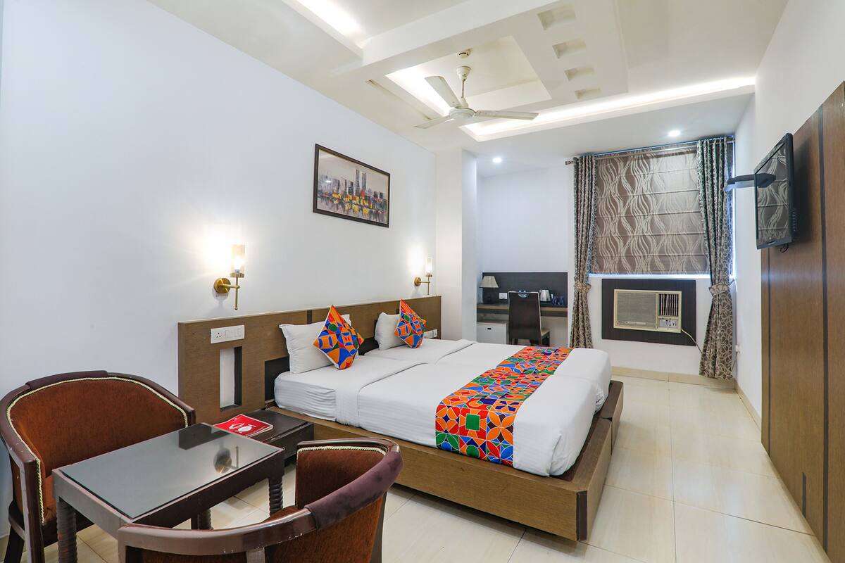 A hotel room with a bed, a desk, a chair, a television, and a window with curtains.