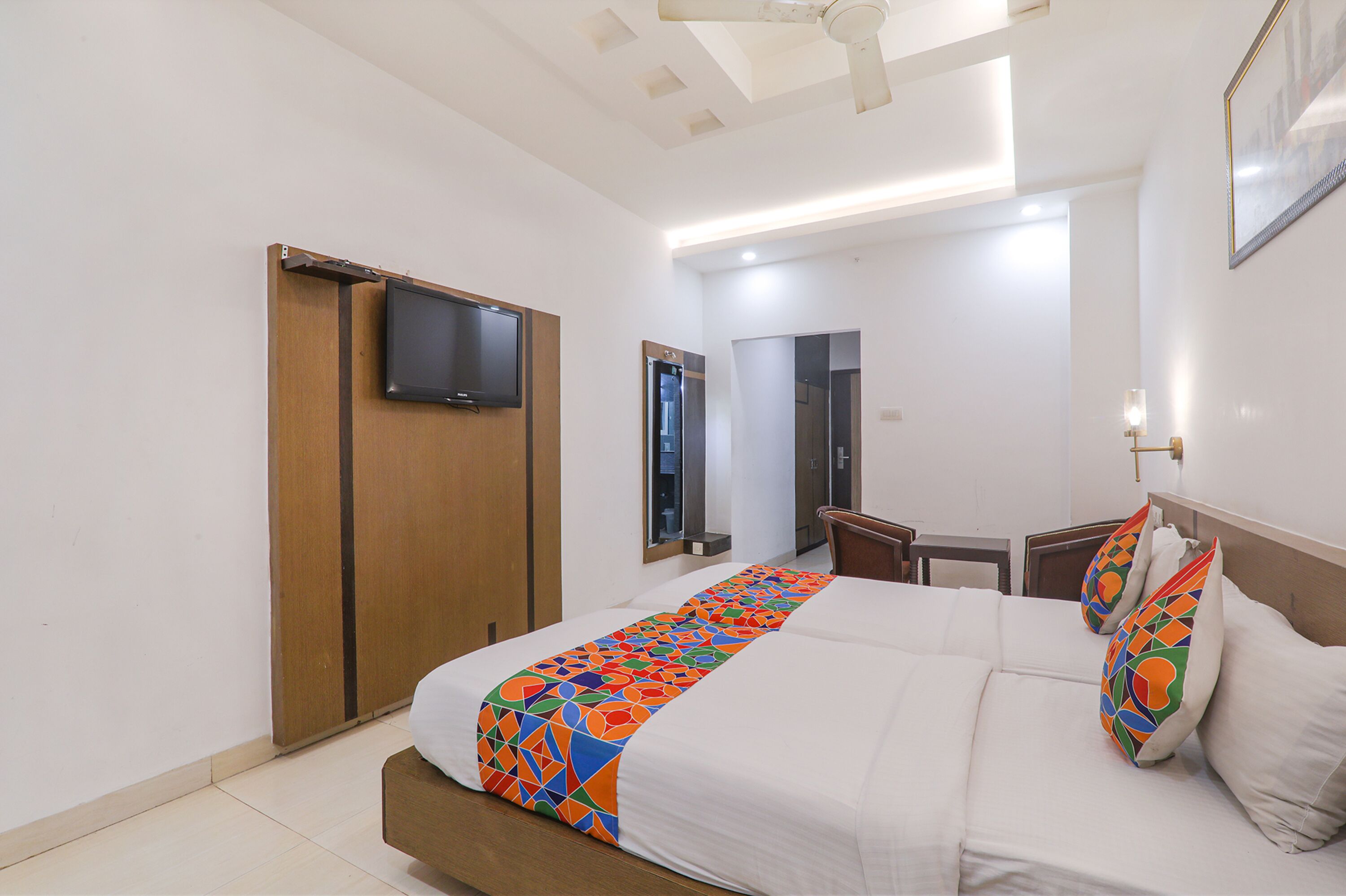 Una habitación de hotel con cama, televisor montado en la pared, armario de madera y escritorio con silla.