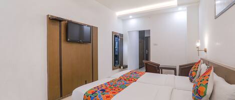 Una habitación de hotel con cama, televisor montado en la pared, armario de madera y escritorio con silla.