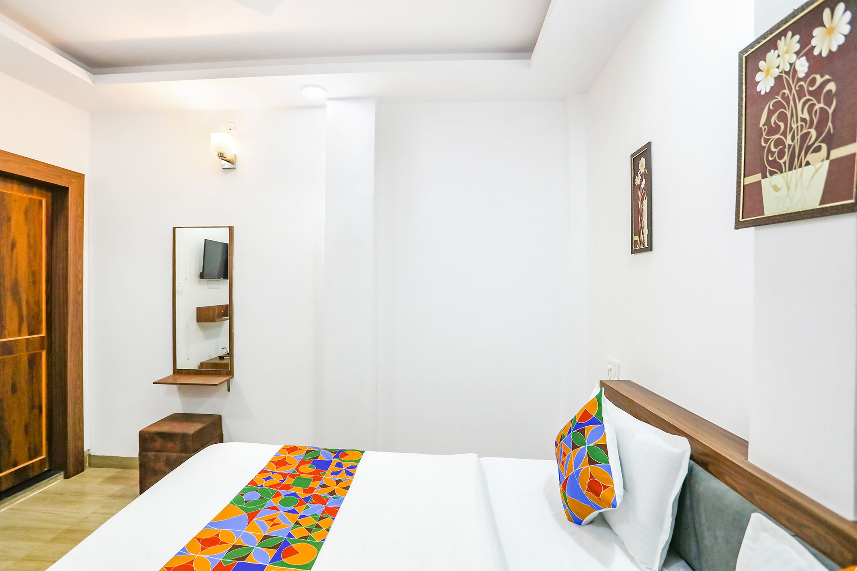 A hotel room with a bed, a wooden headboard, a mirror, and a wall-mounted light fixture.