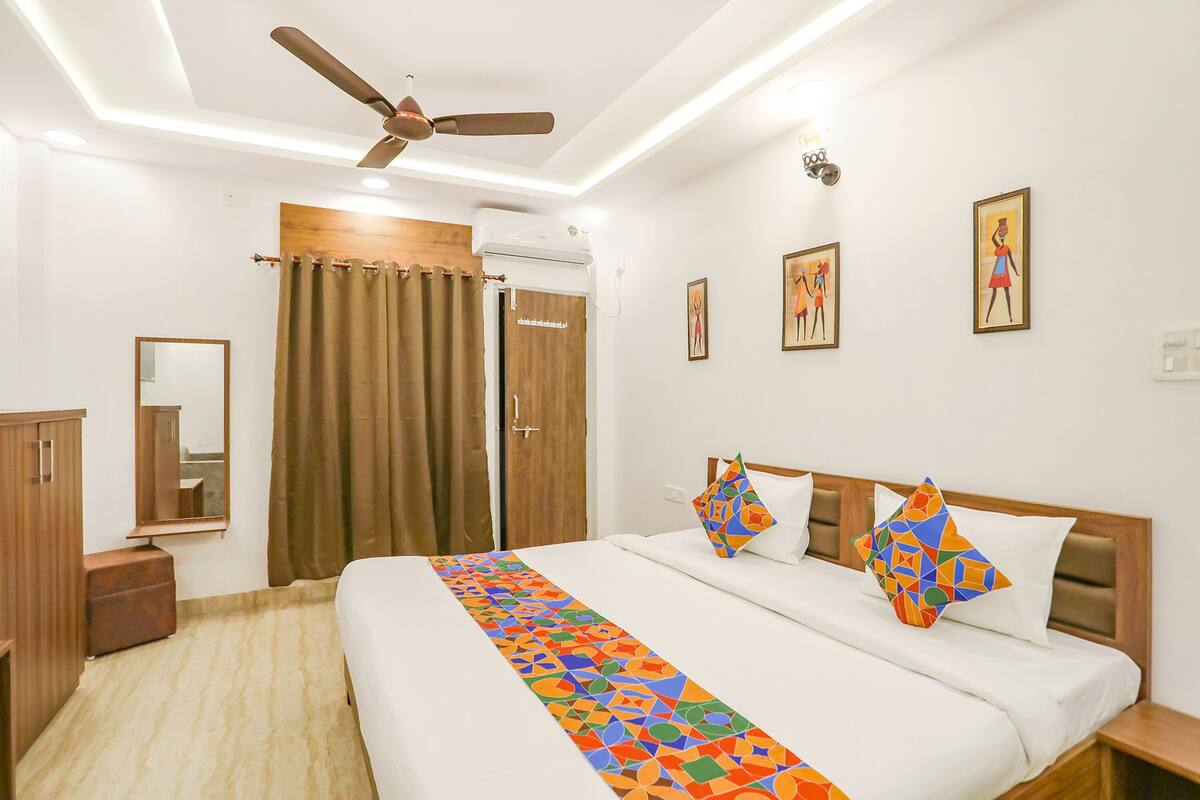A hotel room with a bed, a ceiling fan, a mirror, a wardrobe, and a window with curtains.