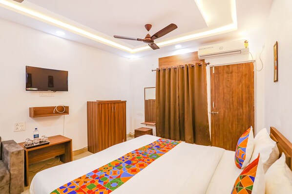 A hotel room with a bed, a ceiling fan, a TV, a wardrobe, a mirror, and an air conditioning unit.