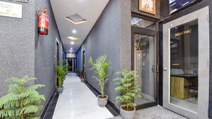 Un couloir d’hôtel orné de plantes en pot, avec un extincteur et une pancarte indiquant le bureau du directeur.