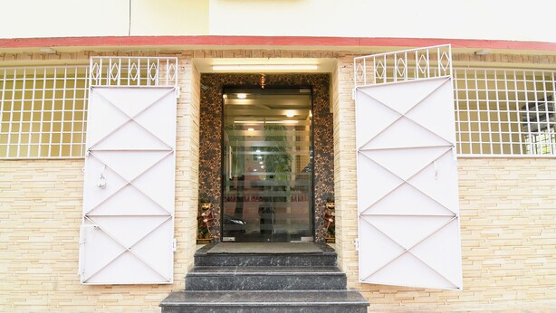 A building entrance with a glass door, two white metal gates, and a brick wall. - Fabhotel Olive Inn I (Barasat)