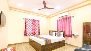 A hotel room with a bed, a ceiling fan, an air conditioning unit, a table with a remote control, and a chair. - Fabhotel Olive Inn I (Barasat)