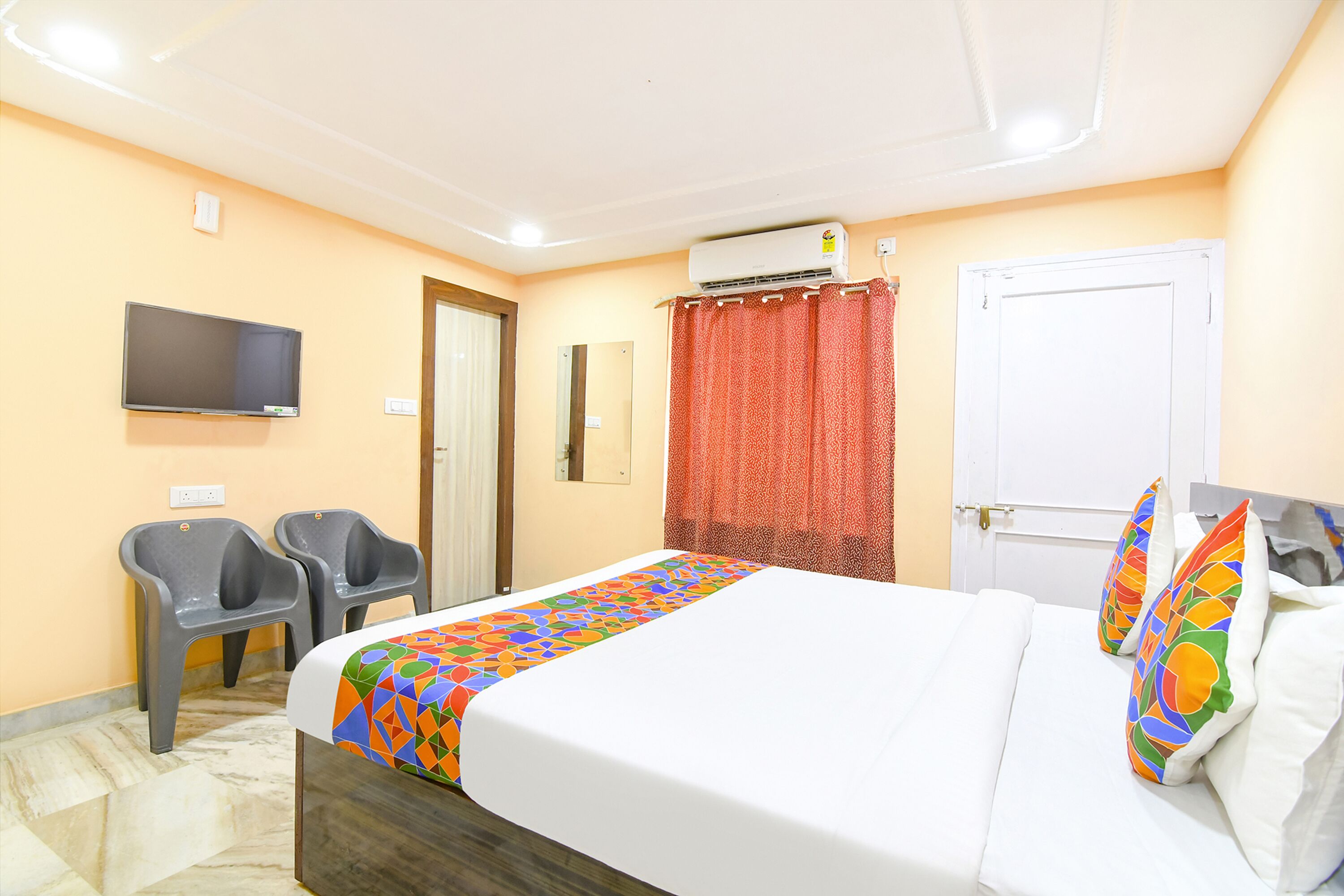 A hotel room with a bed, two chairs, a TV, an air conditioner, and a door.