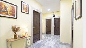 A hallway with a marble floor, framed artwork on the walls, a console table with books and a lamp, and two doors. - Fabhotel Olive Inn I (Barasat)