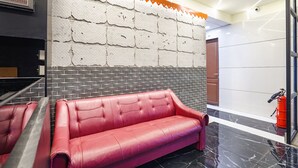 A red leather sofa in a lobby with a textured wall and a fire extinguisher. - Fabhotel Niraant (Surat)