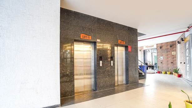 A modern lobby with two elevators marked 'LIFT-5' and 'LIFT-6', a brick wall, and a staircase leading to a second floor. - Fabhotel Niraant (Surat)