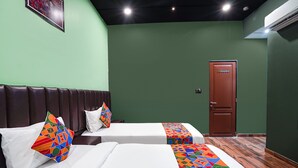 A hotel room with two beds, green walls, a wooden floor, and a door. - Fabhotel Niraant (Surat)