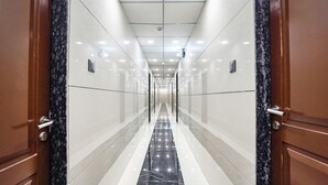 A corridor with a shiny marble floor and wooden doors, leading to a bright, well-lit hallway. - Fabhotel Niraant (Surat)
