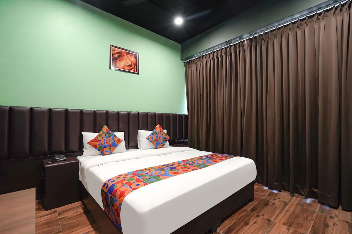 A hotel room with a large bed, a headboard, a nightstand, a telephone, a picture on the wall, and a window with curtains.
