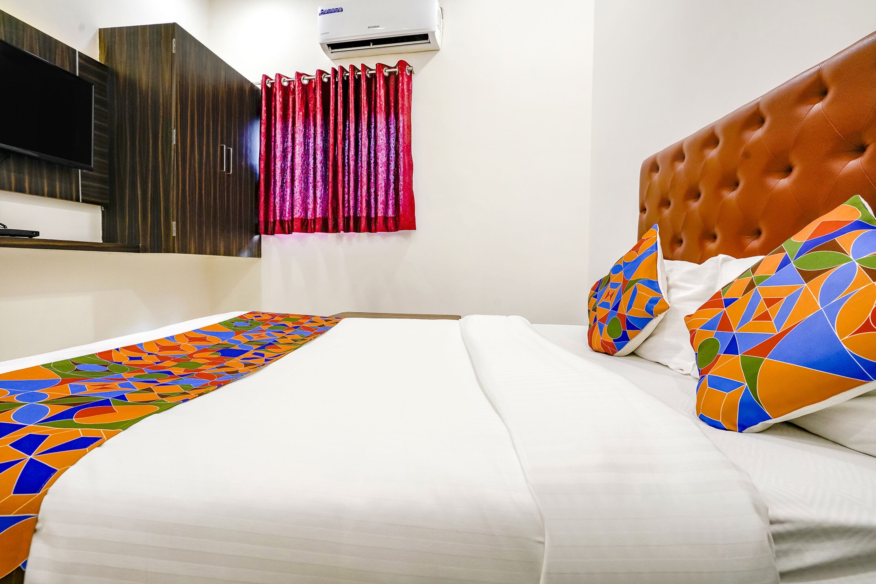 A hotel room with a bed, a TV mounted on the wall, and an air conditioning unit.
