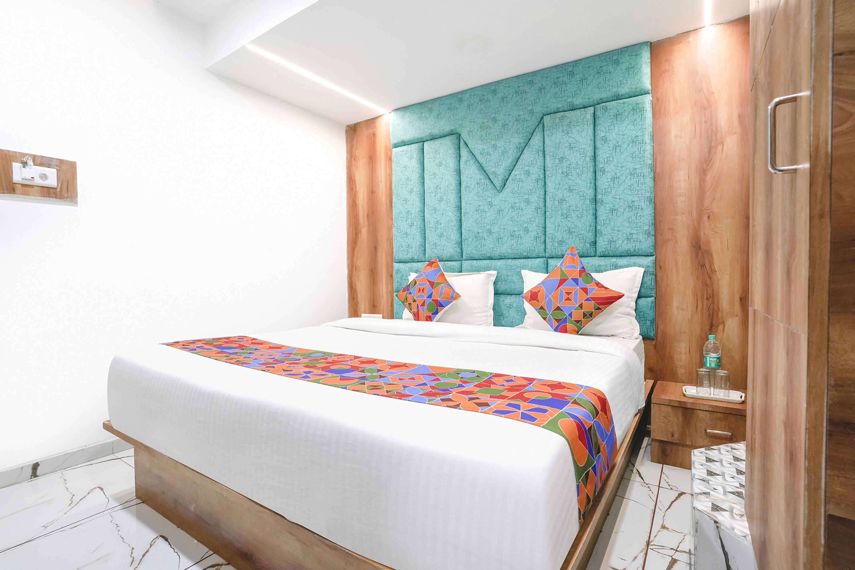 A modern hotel room with a large bed, a teal headboard, and a wooden wardrobe.