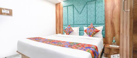 A modern hotel room with a large bed, a teal headboard, and a wooden wardrobe.