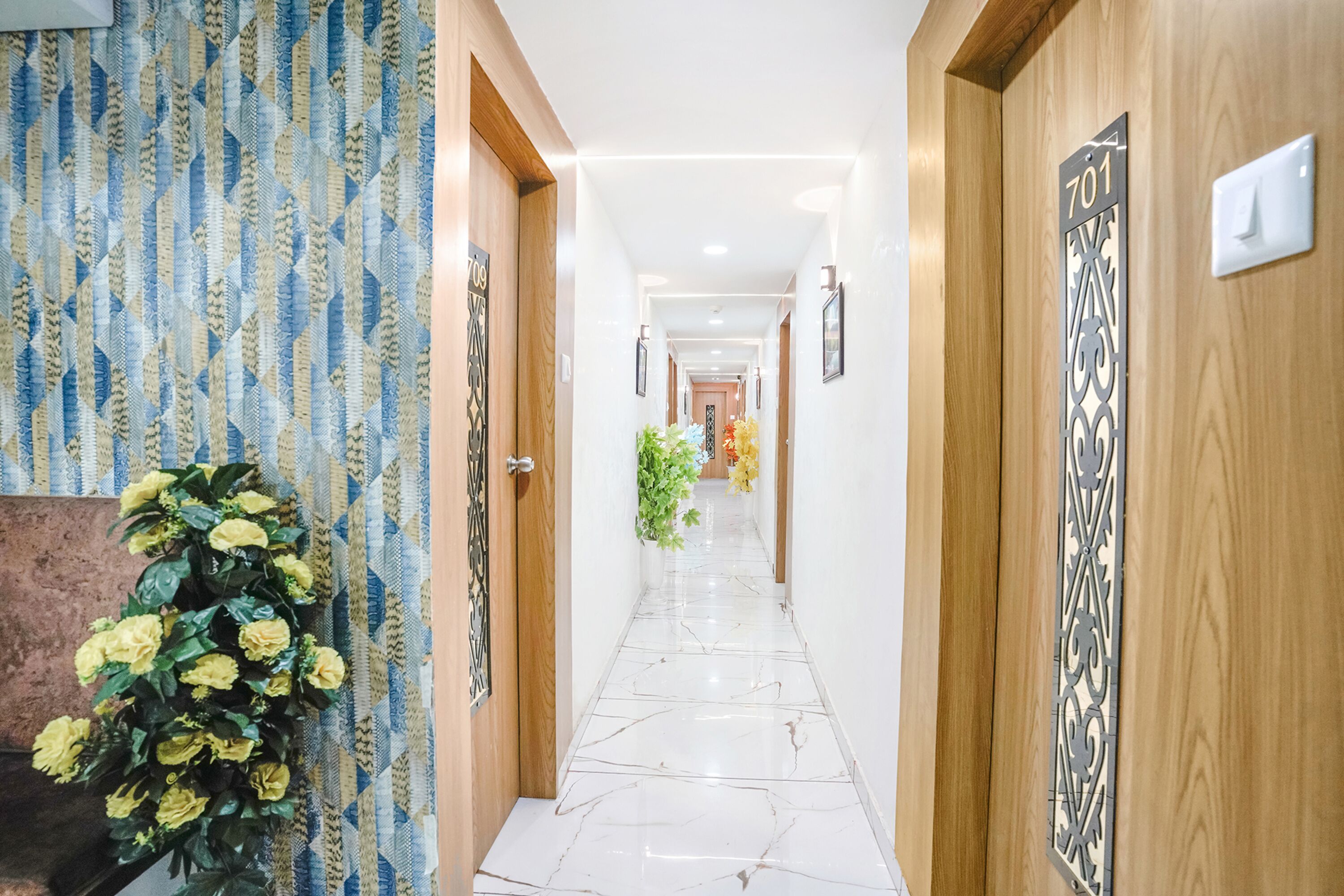 Un couloir d'hôtel avec un papier peint à motifs, une plante en pot et un panneau indiquant le numéro de la chambre sur le mur.