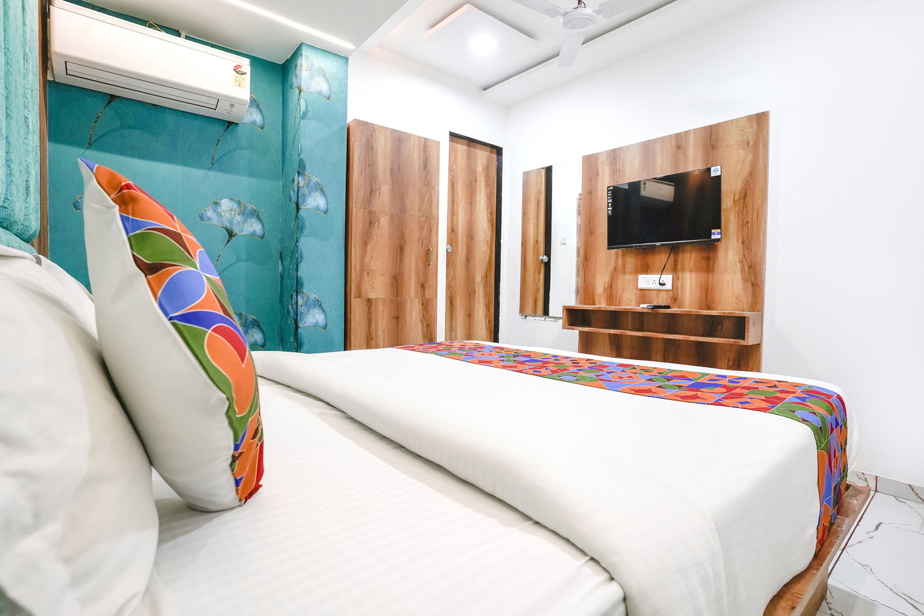 A bedroom with a bed, a TV mounted on the wall, and a wooden wardrobe.