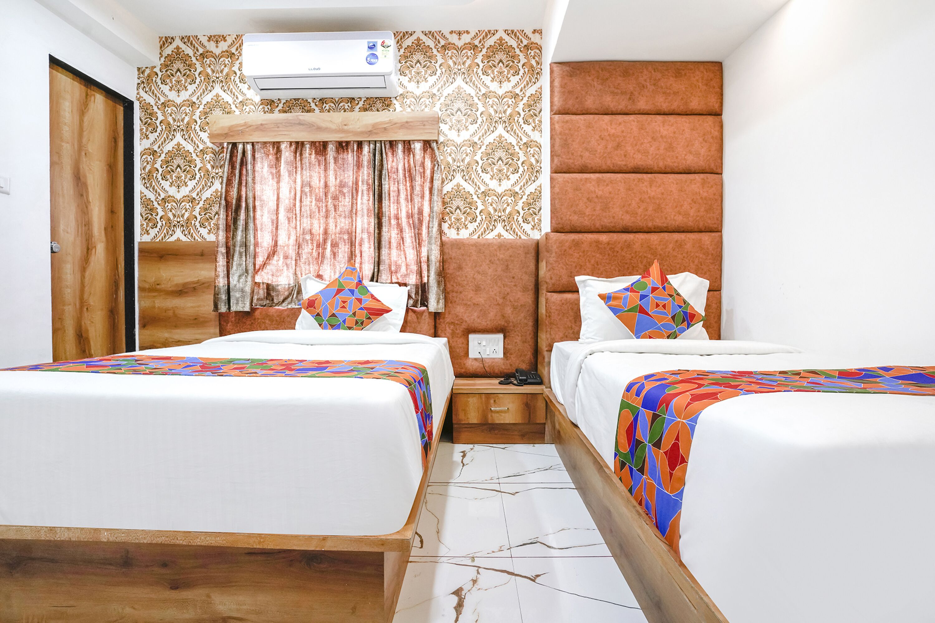 Een hotelkamer met twee bedden, een houten hoofdbord, behang met een patroon en een airconditioningsysteem.