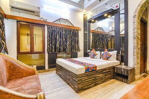 A bedroom with a large bed, a wooden headboard, a sofa, and a mirror. - Fabexpress Avenue Villa (Bidhannagar)