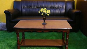 Una mesa de centro de madera con un jarrón de flores amarillas frente a un sofá de cuero negro.