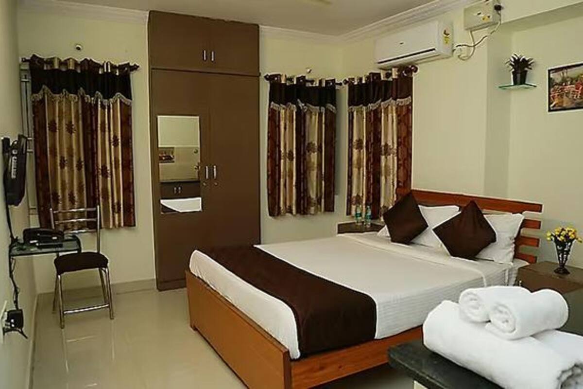 A hotel room with a bed, a desk, a chair, a wardrobe, and an air conditioning unit.