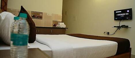 A hotel room with a bed, a bedside table with a water bottle, a TV mounted on the wall, and a mirror above the bed.