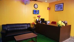 Zona de recepción con un sofá de cuero negro, un mostrador de madera, un reloj y un cuadro en la pared.