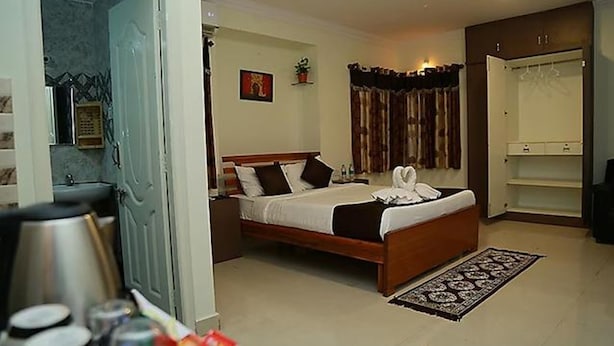 Habitación de hotel con cama, mesita de noche, espejo, armario y baño visible a través de una puerta abierta.