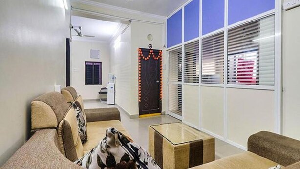 A hotel room with a sofa, a small table, and a window with blinds. - Fabexpress Bb Suites (Hyderabad)