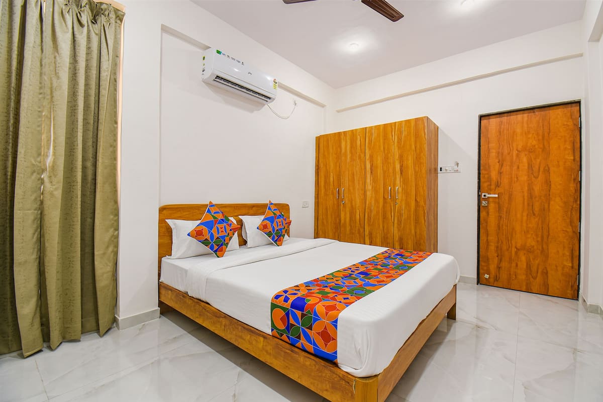 Uma cama bem arrumada com um cobertor colorido, um guarda-roupa de madeira e uma porta fechada em um quarto bem iluminado, com paredes brancas e chão de azulejos.
