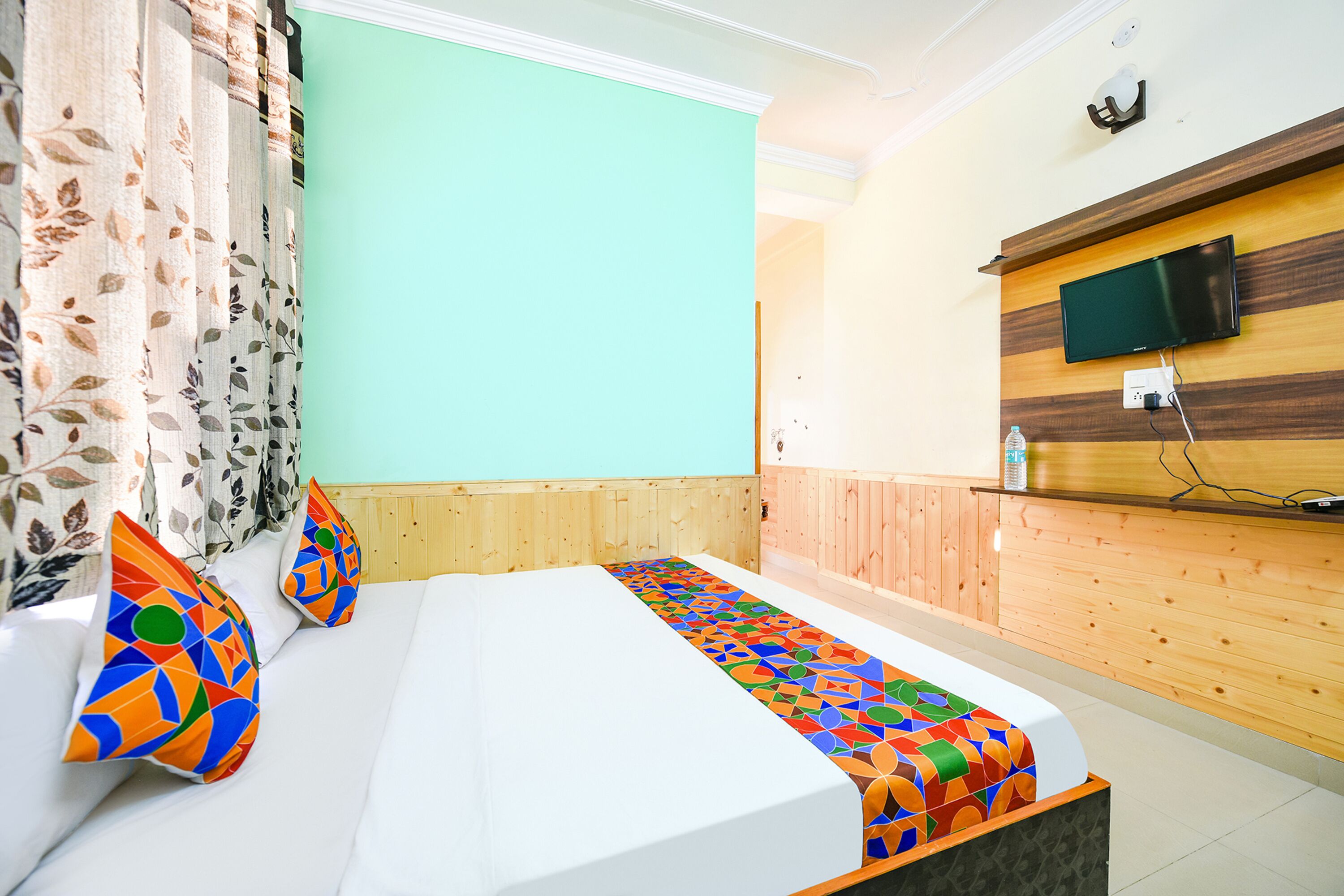 Quarto de hotel com uma cama, televisão fixada na parede e painéis de madeira.