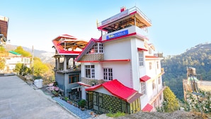 Un immeuble à plusieurs étages, doté d’un toit rouge, portant les inscriptions « Maa Tara Anchal Cottage » et « fab hotels ». Il possède un balcon à l’étage supérieur et un escalier menant à l’entrée.
