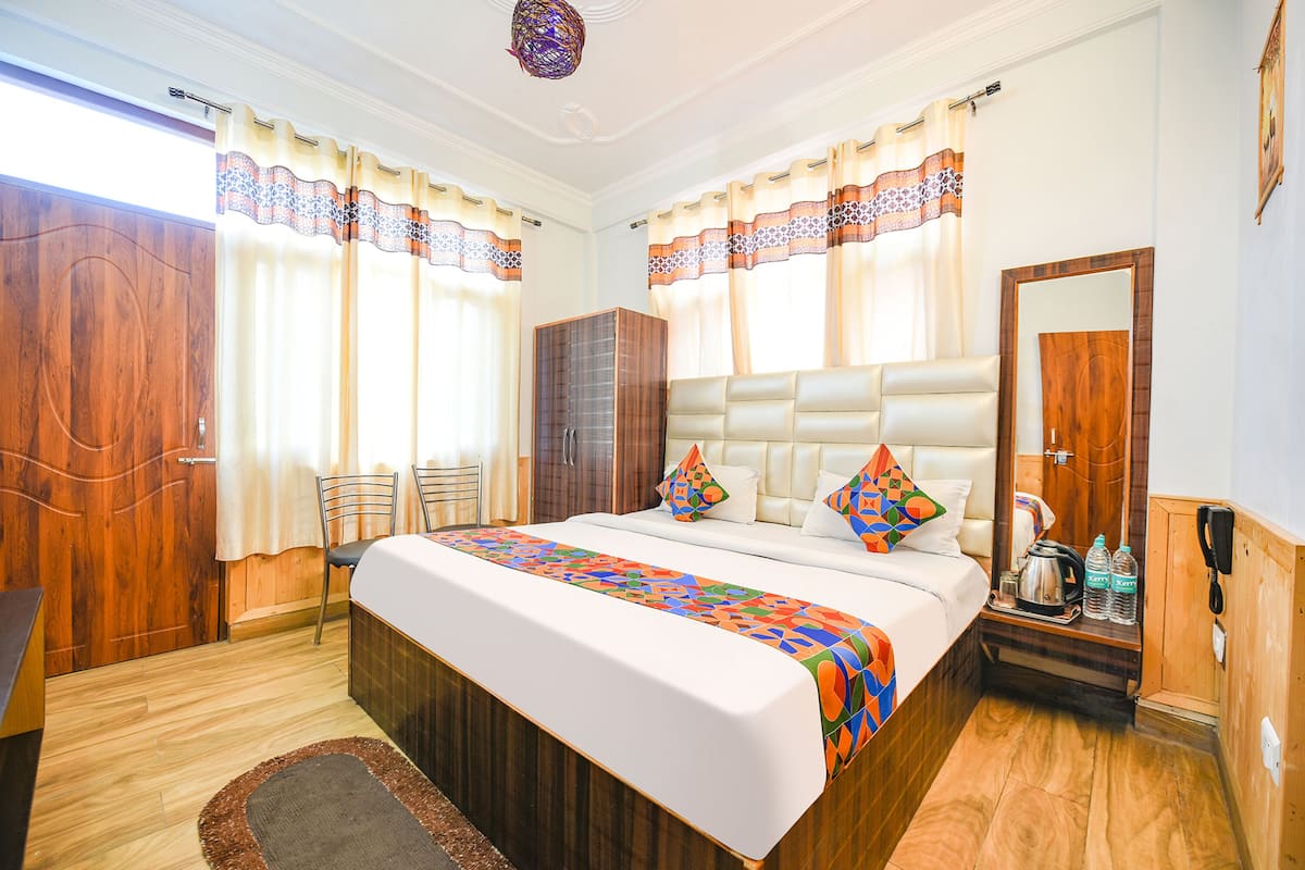 A bedroom with a large bed, a wooden wardrobe, a bedside table with a kettle and bottles, and a mirror.