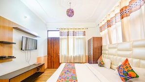 Une chambre d’hôtel avec un grand lit, un téléviseur fixé au mur, une armoire en bois et une fenêtre avec des rideaux.