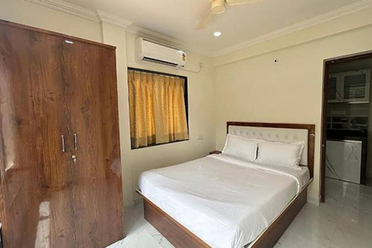 A bedroom with a bed, a wardrobe, an air conditioning unit, and a view of a kitchen area.
