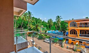 A balcony with a view of a street, palm trees, and a two-story building with a balcony. - Fabhotel De Joe Philips Heights (Arpora)