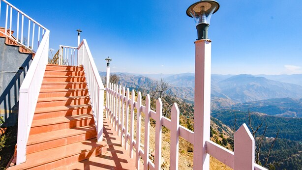 Una escalera con barandillas blancas que lleva a un mirador con vistas a un paisaje montañoso.
