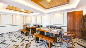 Un comedor con mesas y bancos de madera, piso estampado y techo de madera con iluminación empotrada.
