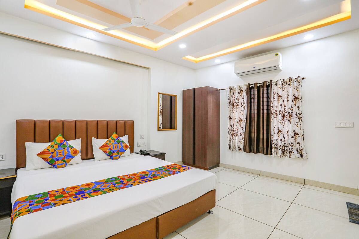A modern hotel room with a large bed, a wardrobe, an air conditioning unit, and a ceiling fan.