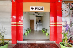Enter a grand space with a reception desk and staircase, surrounded by potted plants and flanked by pillars.