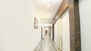 Un pasillo largo y estrecho con piso pulido, paredes blancas y un panel de madera a la derecha.