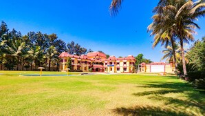 Un hotel grande de varios pisos con techo rojo y paredes amarillas, rodeado de palmeras y un césped bien cuidado.