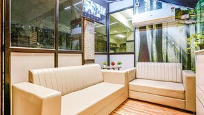 A corner seating area with a sofa and a chair, a small table with plants, and a large window with a view of trees. - FabHotel Eminent Suites Banjara Hills - Nr. LV Prasad EYE Institute (Hyderabad)