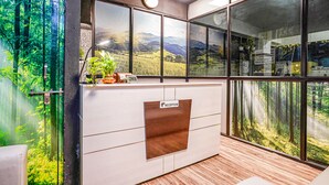 A reception desk with a view of a forest through large windows. - FabHotel Eminent Suites Banjara Hills - Nr. LV Prasad EYE Institute (Hyderabad)