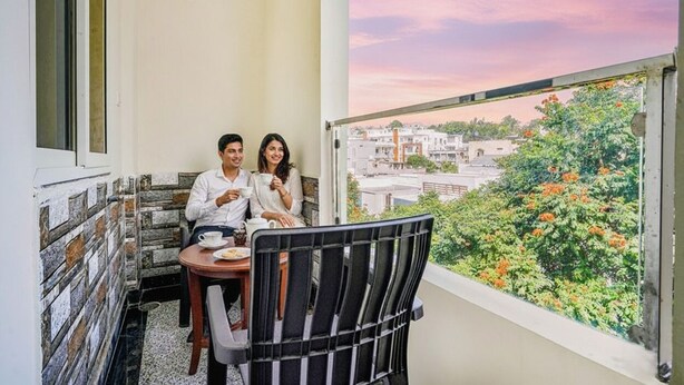 A balcony with a city view, a table with chairs, and a window with a view of buildings and greenery. - FabHotel Eminent Suites Banjara Hills - Nr. LV Prasad EYE Institute (Hyderabad)