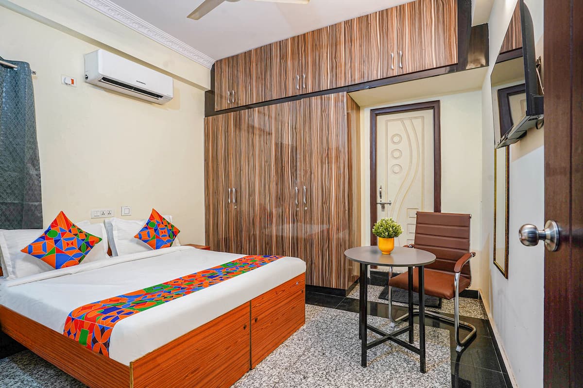 Habitación de hotel con cama, una mesita pequeña con una silla, unidad de aire acondicionado y una puerta con panel decorativo.