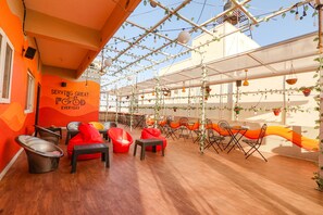 A rooftop dining area with wooden flooring, red and black chairs, and hanging plants. - Fabhotel Lavish Palms (Hyderabad)