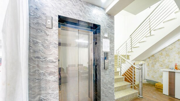 Un ascensor con pared de mármol, una escalera con barandilla y un mostrador de recepción.